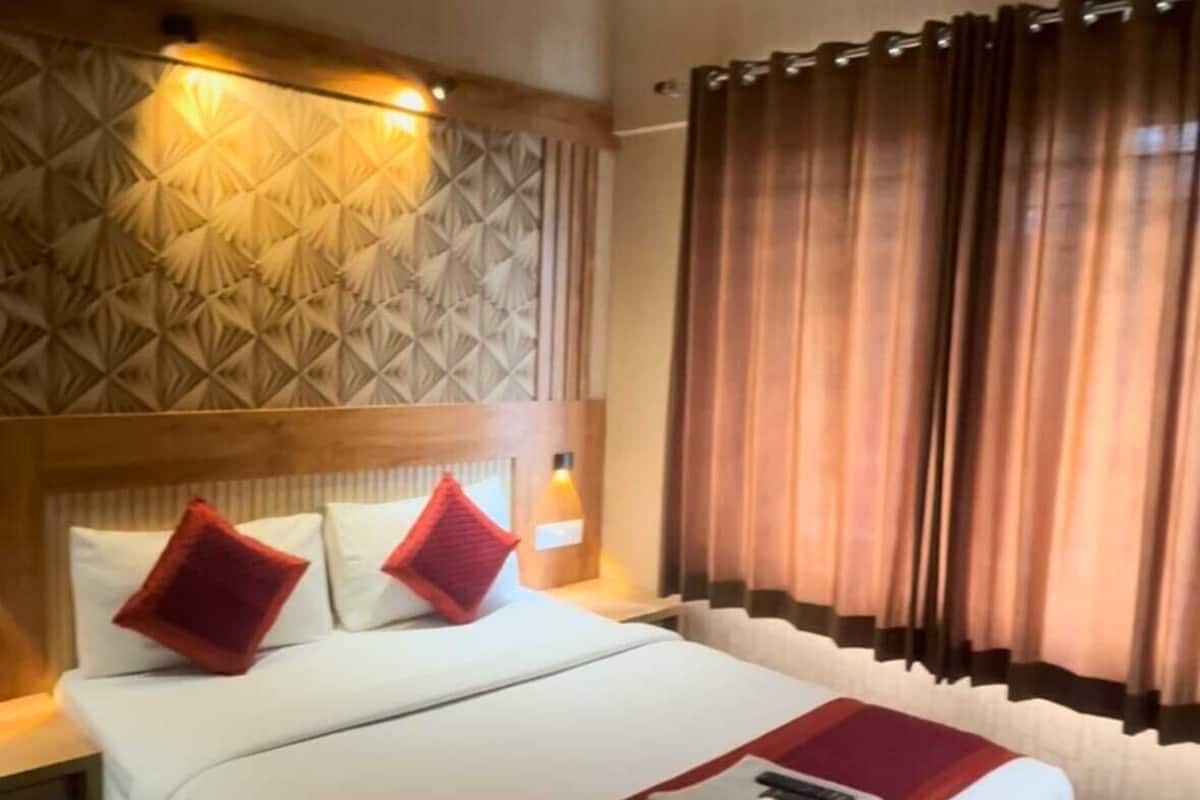 Une chambre d’hôtel avec un lit, un ventilateur de plafond, un mur décoré de motifs et une fenêtre avec des rideaux.