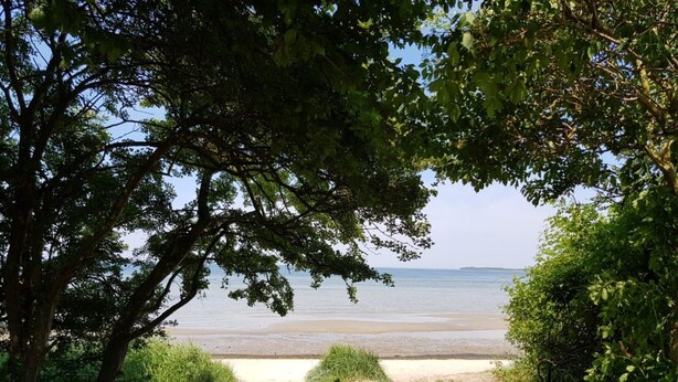 En stig som leder till en strand med utsikt över havet och det avlägsna landskapet.