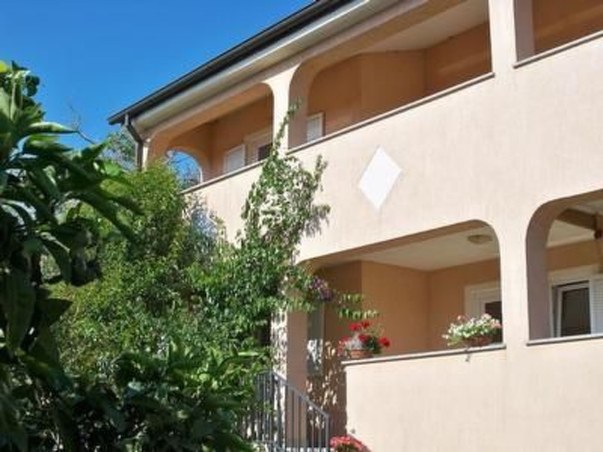 A multi-story building with balconies, large windows, and a garden area with plants and flowers.