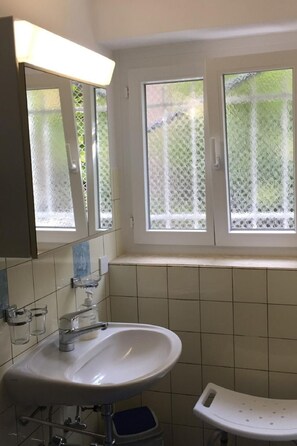 Un baño con lavamanos blanco, un espejo y una ventana con cortina de encaje.