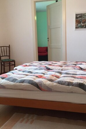 Un dormitorio con cama, una silla, una puerta y un cuadro en la pared.