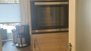 Eine kompakte Küche mit Holzschränken, einem eingebauten Backofen und einer Kaffeemaschine auf der Arbeitsfläche.
