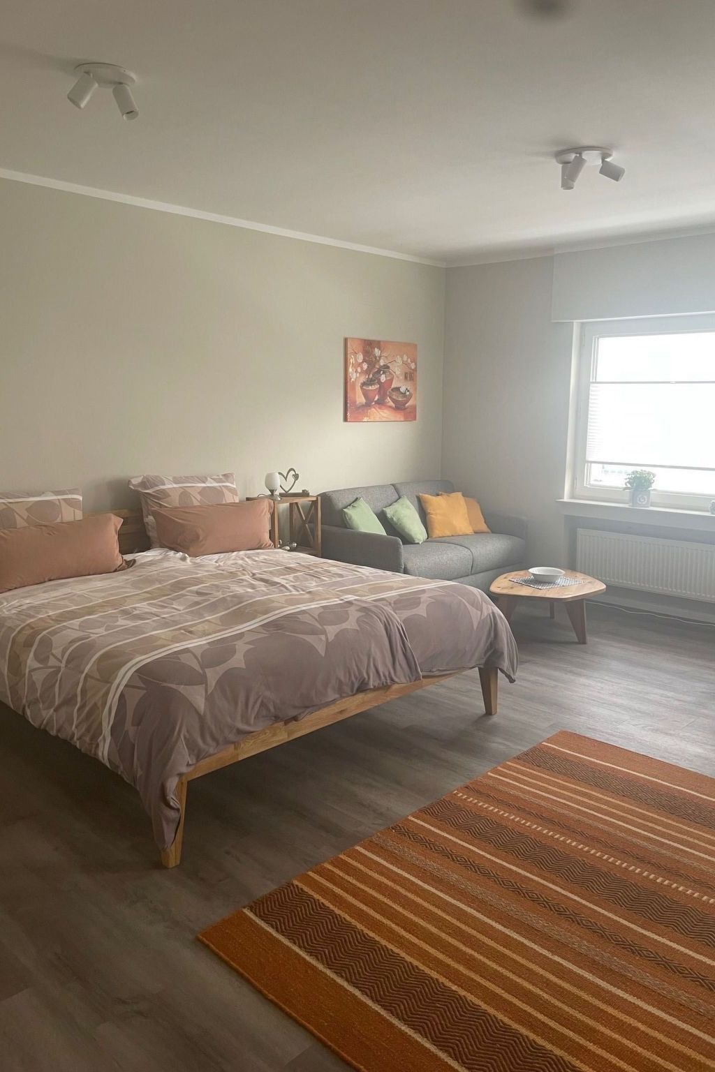Un dormitorio con cama, sofá, una mesita y una ventana.