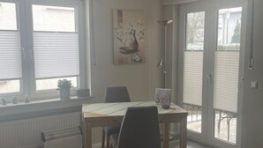 Ein Essbereich mit Tisch und Stühlen, einem Heizkörper und einem Fenster mit Jalousien.