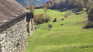 A stone building with a sloped roof overlooking a green valley with trees and mountains in the background. - Rustico Monti di Rima by Interhome (Broglio)