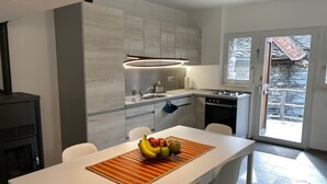 A modern kitchen with a built-in stove, a dining area with a table set for two, and a view of a stone building outside. - Rustico Monti di Rima by Interhome (Broglio)