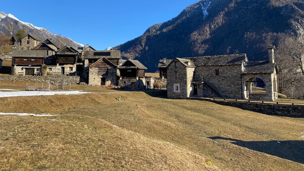 A traditional stone building with a wooden facade, set against a backdrop of snow-capped mountains and clear blue sky. - Rustico Monti di Rima by Interhome (Broglio)