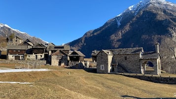 Ein traditionelles Steinhaus mit Holzfassade, vor einer Kulisse aus schneebedeckten Bergen und blauem Himmel.