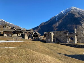 Un edificio de piedra tradicional con fachada de madera, con montañas nevadas y cielo azul despejado al fondo.