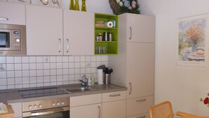 Een keuken met witte kastjes, een magnetron, een oven en een groene plank met keukenspullen.