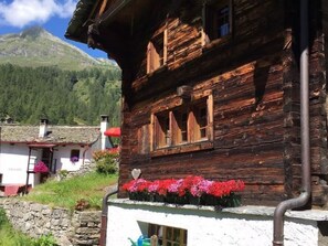 Un bâtiment rustique en bois, avec des fondations en pierre, des volets en bois et une jardinière ornée de fleurs rouges.