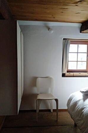 Ein Zimmer mit einem Bett, einem Stuhl und einem Vorhangfenster.