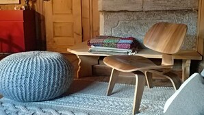 Una habitación acogedora con una silla de madera, un taburete tejido y una mesita con una manta y libros.