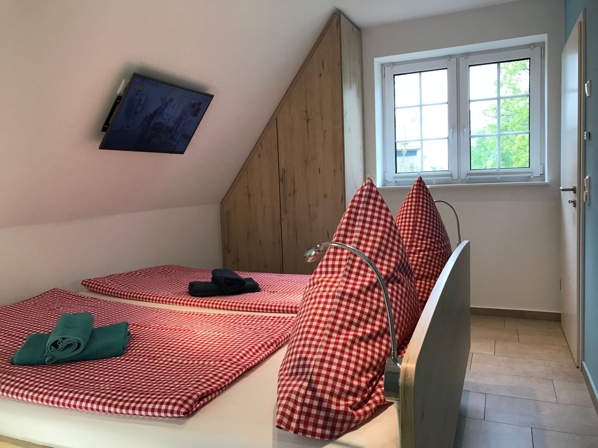 A small bedroom with a bed, a window, and a TV mounted on the wall.