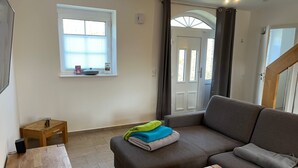 Una sala de estar con un sofá, una mesa de centro, una pequeña mesa de madera, una ventana con persianas y una puerta con cortinas.