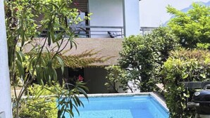 Un área de estar al aire libre con techo y una piscina al fondo.