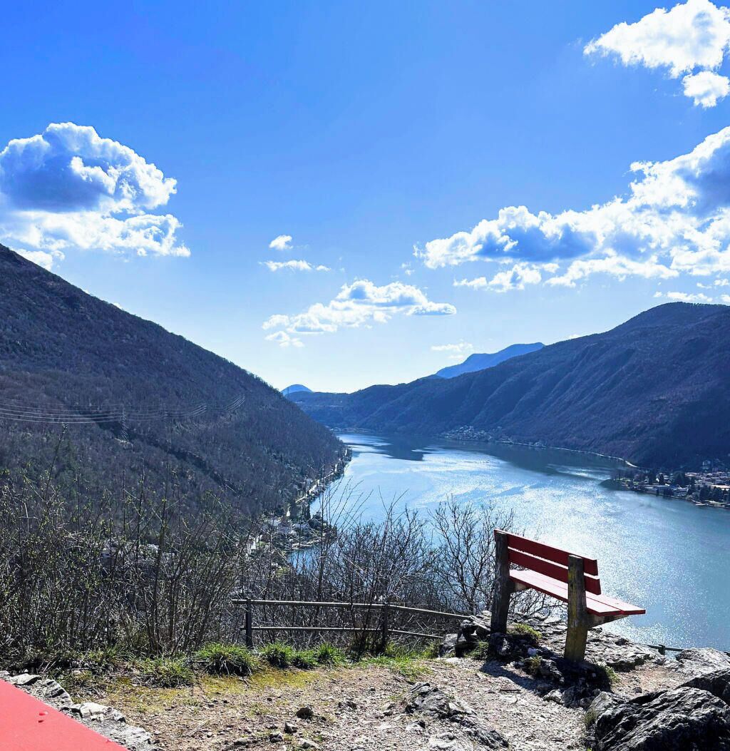 Eine Bank mit Blick auf einen Fluss, im Hintergrund Berge.