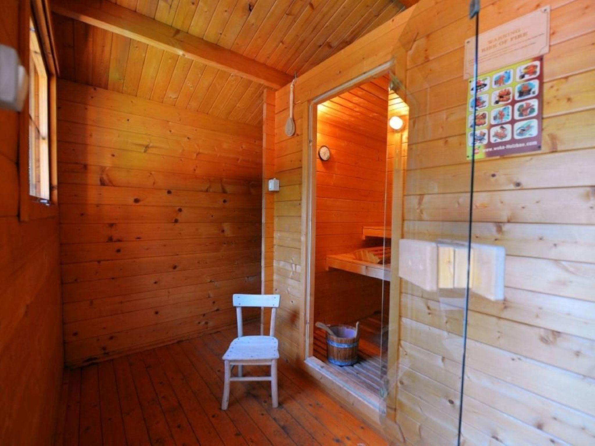 A wooden cabin with a glass door leading to a small bathroom. A white chair is placed inside the cabin.