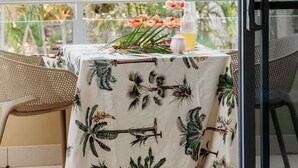 Un balcón con una mesa cubierta con mantel de estampado tropical, sillas y una botella de bebida.