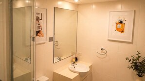 Un baño con cabina de ducha de vidrio, un lavabo con espejo y una botella de perfume enmarcada en la pared.