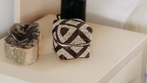 Una mesita de noche con una lámpara, un adorno de madera y un cojín estampado.