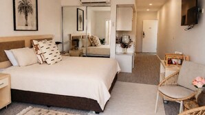 Una habitación de hotel con una cama, una silla, un escritorio, un televisor y un espejo.