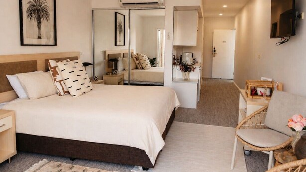 Una habitación de hotel con una cama, una silla, un escritorio, un televisor y un espejo.