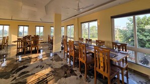 A spacious dining area with wooden tables and chairs, large windows, and a ceiling fan. - Tiger Inn Beach Resort (Mandarmani)