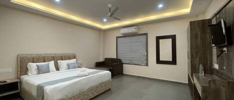 A modern hotel room with a large bed, a ceiling fan, recessed lighting, a window with blinds, and a wooden wardrobe.