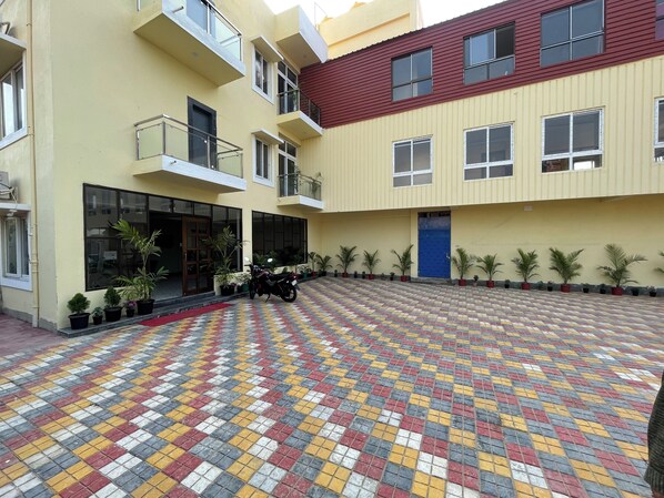 A courtyard with a patterned tiled floor, a motorcycle parked near a building entrance, and potted plants along the walls.