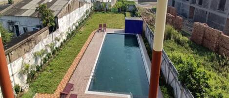 A swimming pool with a wooden deck and lounge chairs, surrounded by greenery and a view of the ocean.