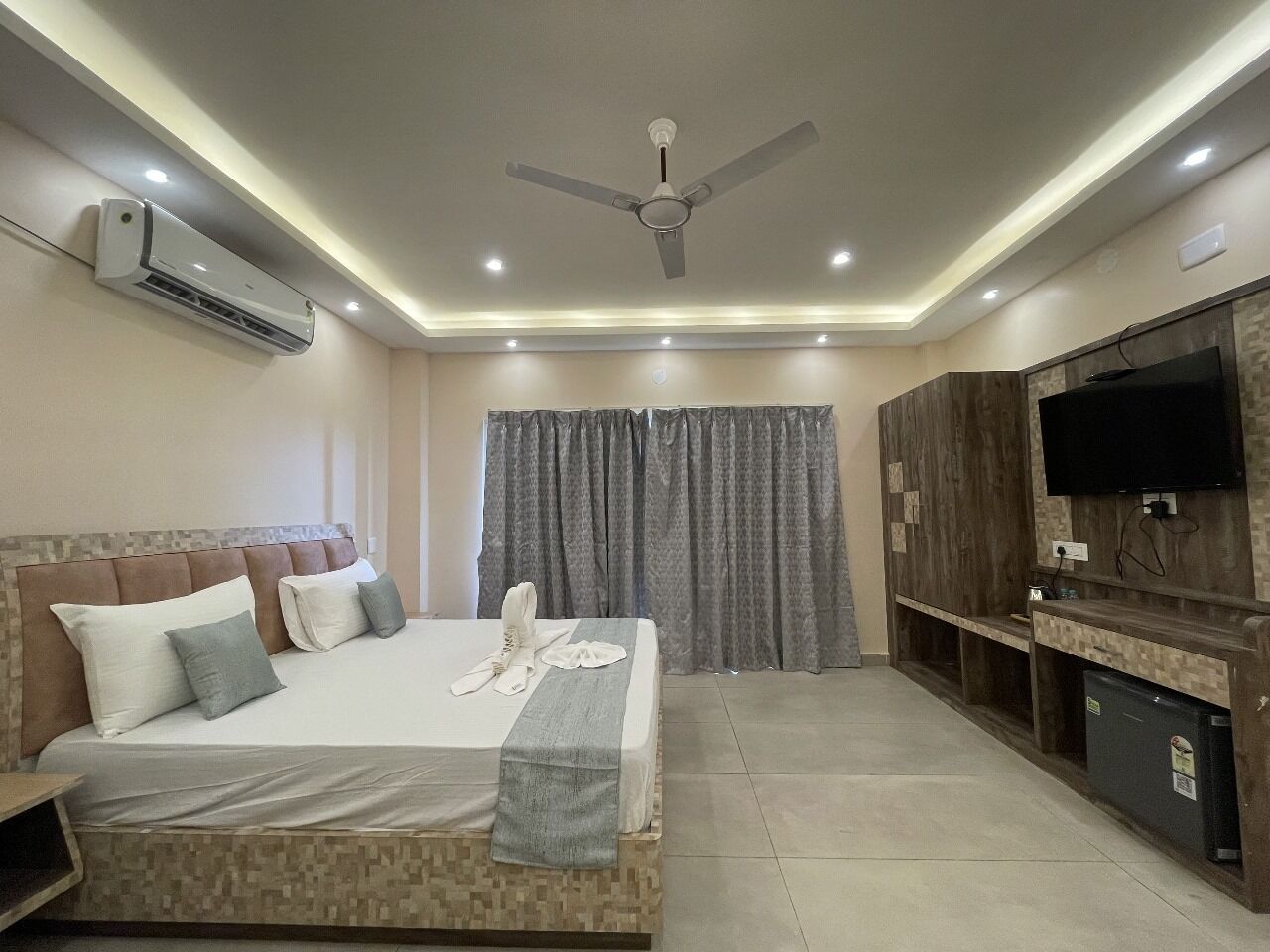 A modern hotel room with a large bed, a flat-screen TV, a ceiling fan, and an air conditioning unit.