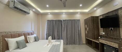 A modern hotel room with a large bed, a flat-screen TV, a ceiling fan, and an air conditioning unit.