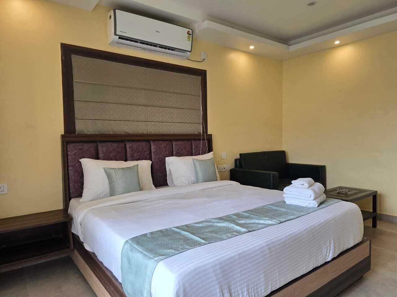 A hotel room with a large bed, a headboard, a TV, and a bedside table with towels.