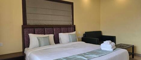 A hotel room with a large bed, a headboard, a TV, and a bedside table with towels.