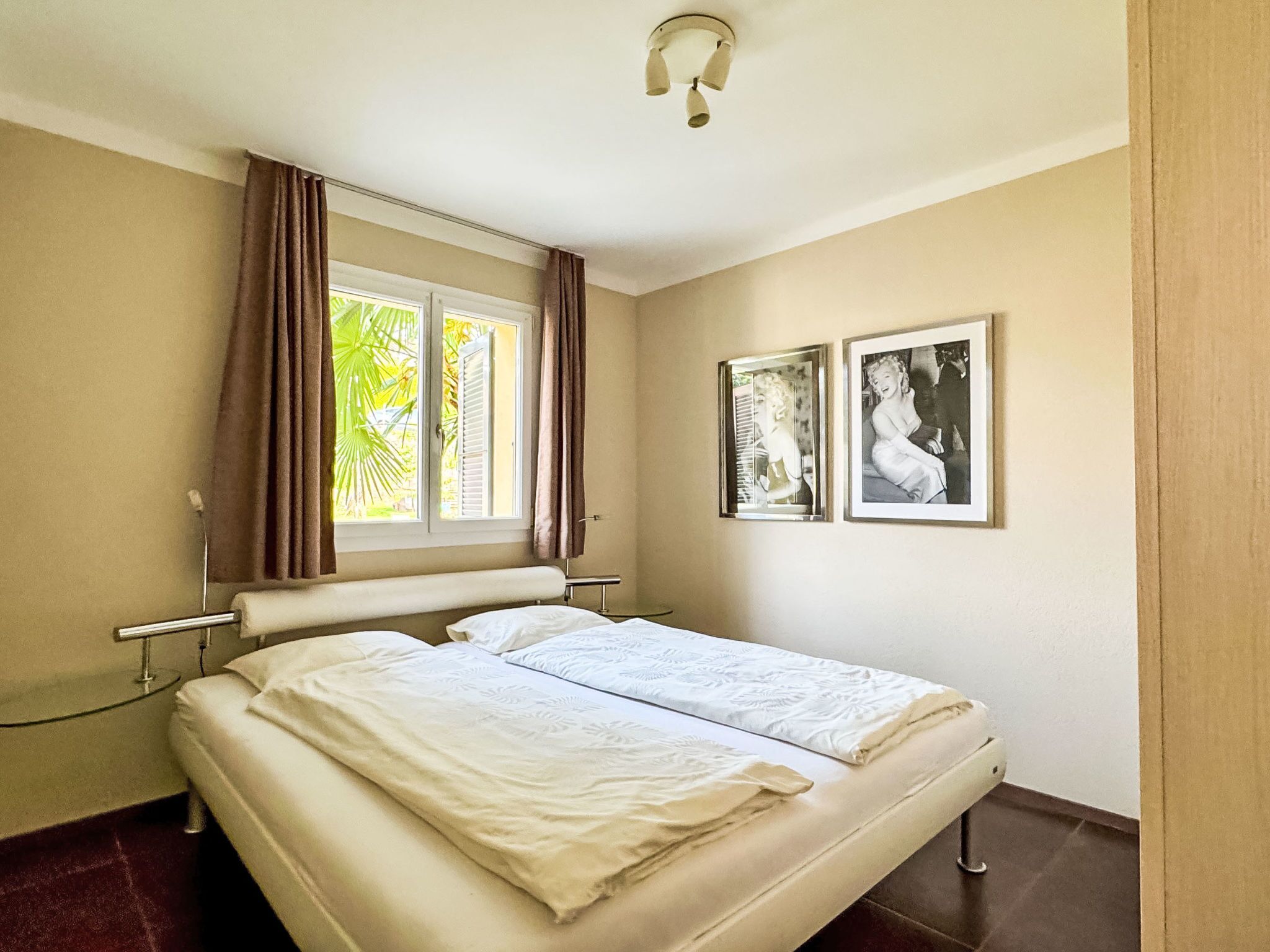 Ein Doppelbett mit weißer Bettwäsche, ein Fenster mit Vorhängen und zwei gerahmte Bilder an der Wand.