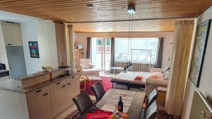 Ein Hotelzimmer mit Esstisch, Stühlen, einer Couch, einer Küchenzeile und einem Balkon mit Aussicht.