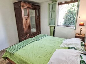A bedroom with a bed, a wooden wardrobe, a window with curtains, and a bedside lamp. - Provence ruhiges haus 2 schlafzimmer by Interhome (Lorgues)