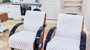 Dos sillas con funda texturizada blanca, una zona de cocina con electrodomésticos y una puerta blanca.