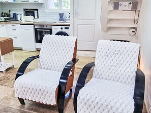 Two chairs with a textured white cover, a kitchen area with appliances, and a white door. - Provence ruhiges haus 2 schlafzimmer by Interhome (Lorgues)