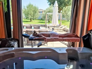 A massage therapy room with a reclining chair, a massage table, and a view of an outdoor patio area with lounge chairs and a pergola. - Hacienda Matea - Oase der Romantik in Strandnähe by Interhome (Pula)
