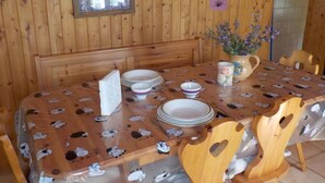 A dining area with a wooden table and chairs, a vase with flowers, and a window with curtains. - Schönes Rustico by Interhome (Dangio – Torre)