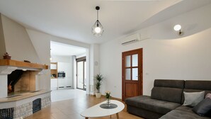 Ein modernes Wohnzimmer mit Kamin, einer Couch, einem Couchtisch und einem Essbereich, im Hintergrund eine Küche.