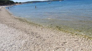 Ein Kiesstrand mit klarem Wasser und Booten.