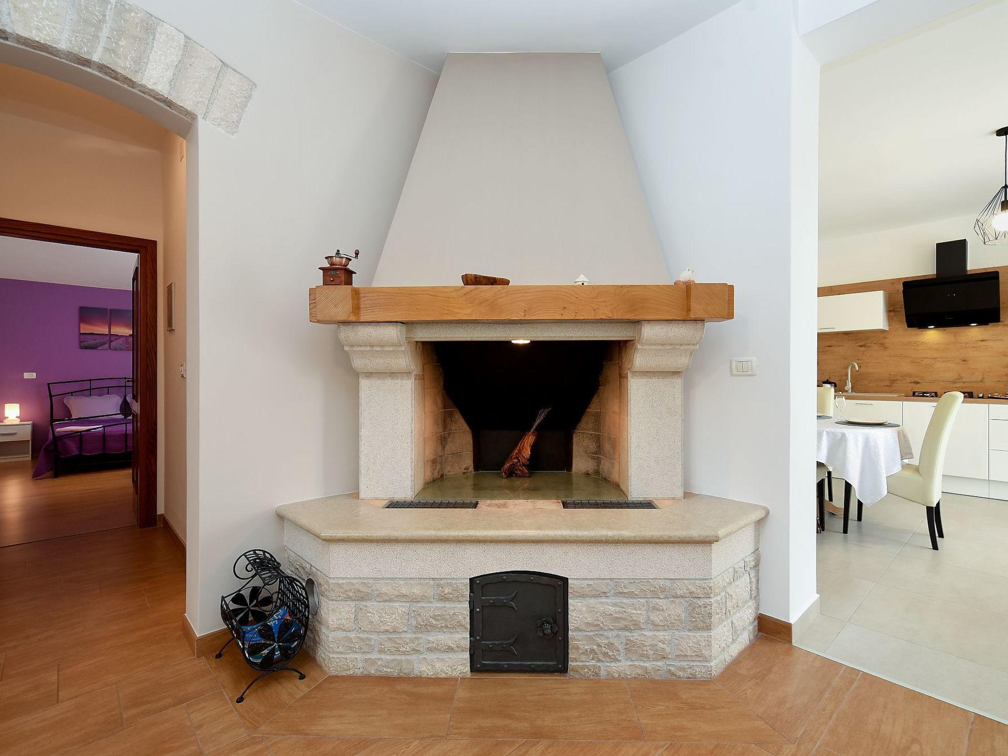 A modern living room with a stone fireplace, a dining area, and a view of a purple-lit room.