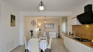 Eine moderne Küche mit weißen Schränken, einer schwarzen Dunstabzugshaube und einem Essbereich mit weißem Tisch und Stühlen.