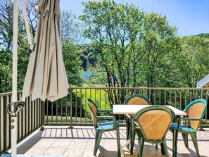 Ein Balkon mit Tisch und Stühlen, einem Sonnenschirm und Blick auf Bäume sowie ein Gebäude im Hintergrund.