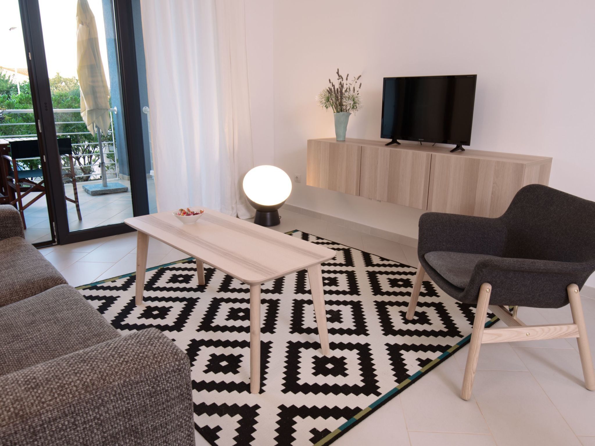 Ein modernes Wohnzimmer mit einer Couch, einem Couchtisch, einem Fernseher auf einer Holzkommode und einem gemusterten Teppich.