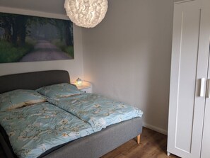 Une chambre à coucher comprenant un lit, une table de chevet, une lampe fixée au mur et une armoire.