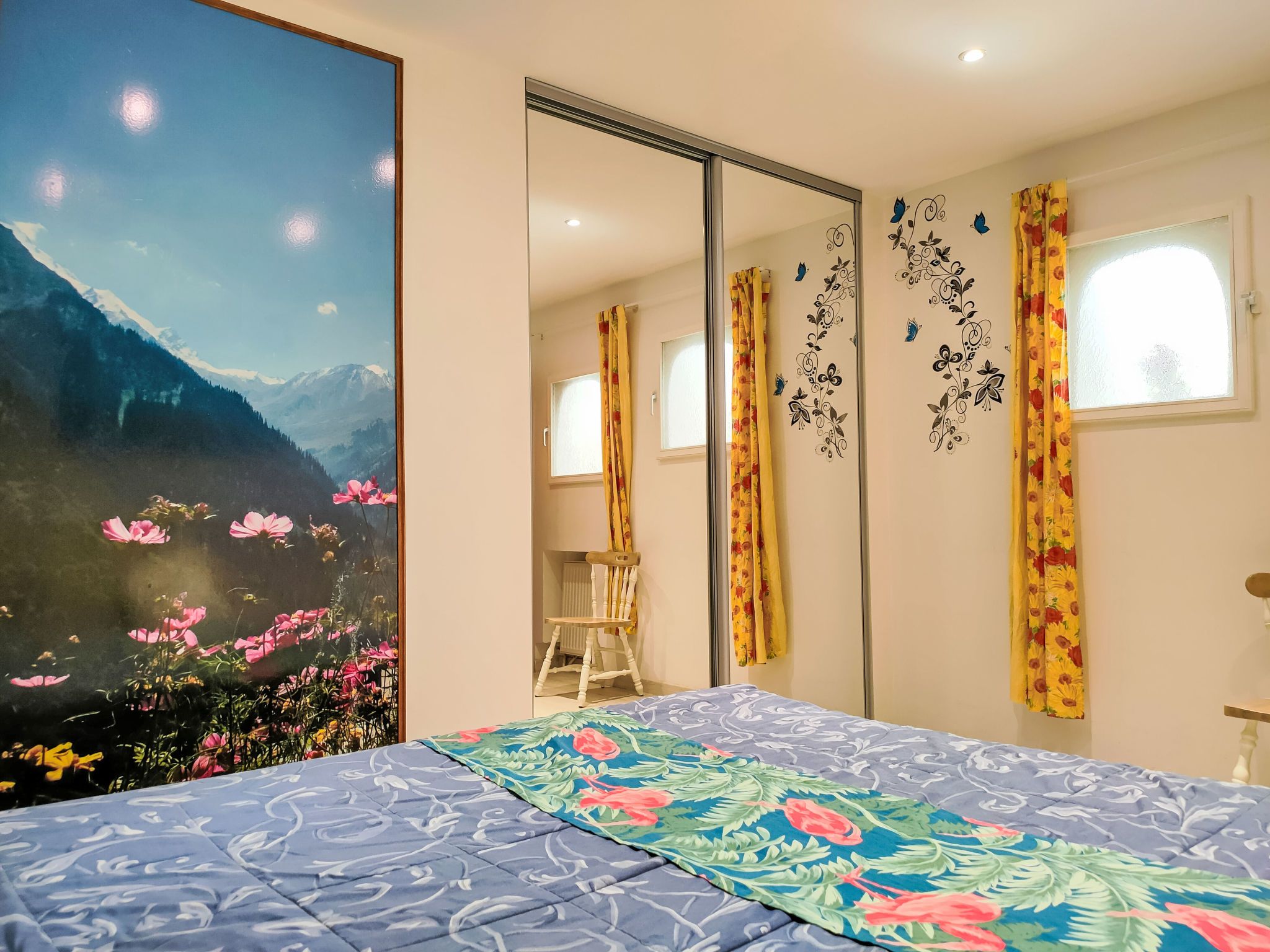 A bedroom with a large bed, a wardrobe, a mirror, and a window with curtains.